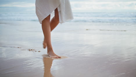 woman feet stepping sea beach closeup. slim legs walking ocean shore in summer