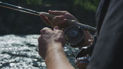 slow motion footage of a fly fisherman with a fish on his line and his reel spooling out and him reeling it in