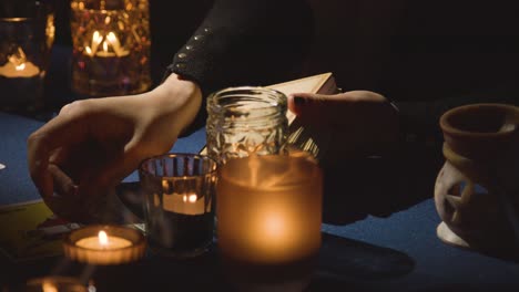 primer plano de una mujer dando una lectura de tarot en una mesa a la luz de las velas sosteniendo una carta de la muerte