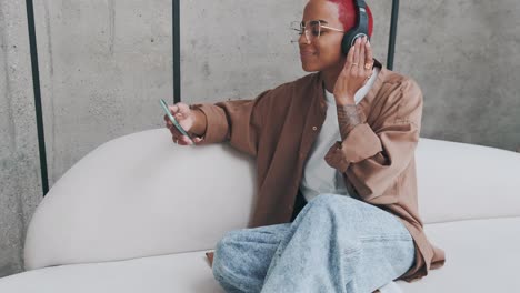 young african american woman listens to music on headphones and holds phone