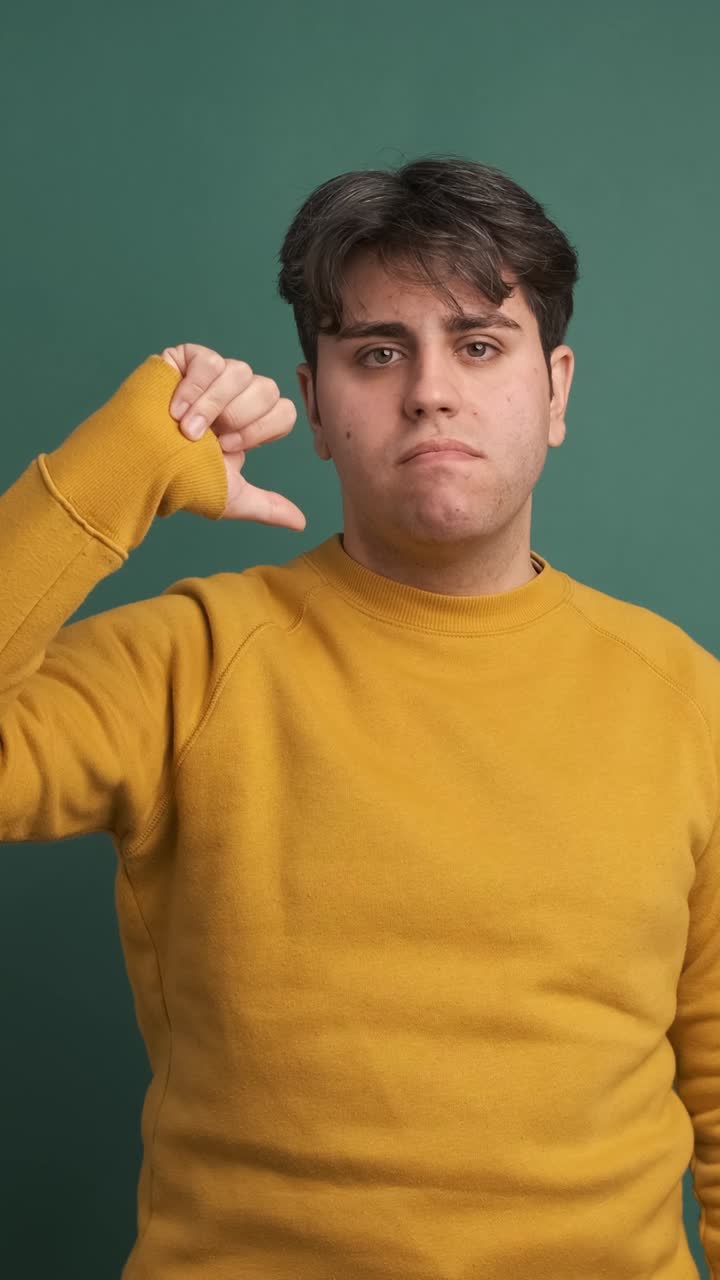 Upset young man gesturing thumb down in green studio