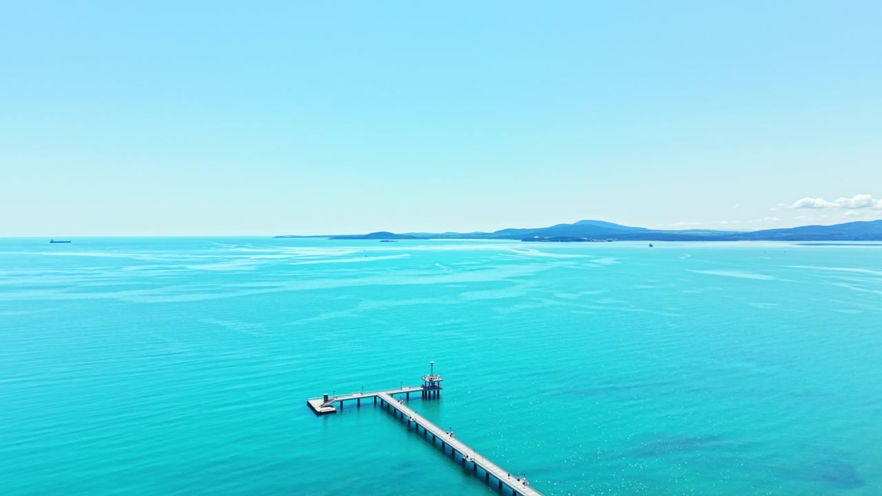 昼間、澄み切った空の下、ブルガスの水面と桟橋の眺め。水平線には遠くの陸地が見える。