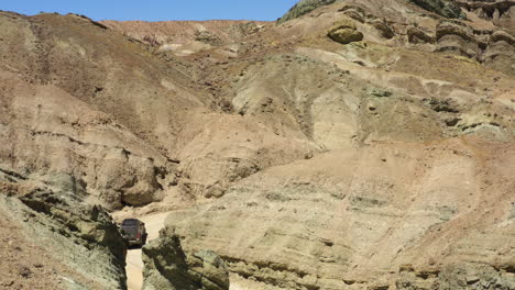 Big-four-by-four-driving-up-winding-gravel-road-leading-through-canyon-in-Rainbow-Basin,-California