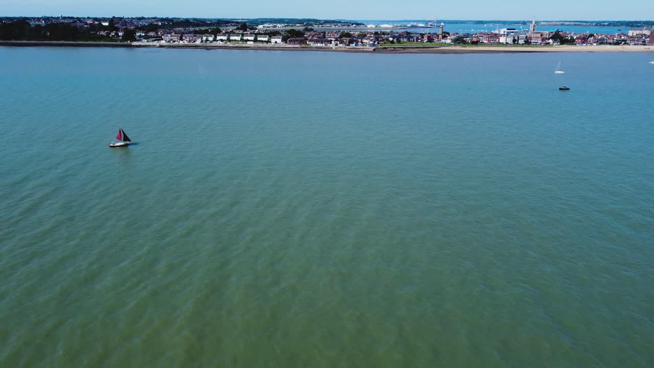 un panorama de la ciudad de harwich, reino unido filmado desde el mar: unos pocos barcos están amarrados cerca de la costa, mientras una ligera brisa sopla al lado de las casas extendidas a lo largo de la costa