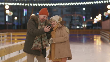 senior couple taking a selfie at an ice rink at night