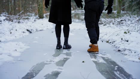 young couple having fun sliding in the snow on ice in park