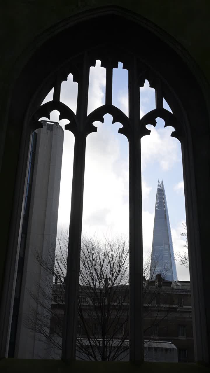 Una prospettiva drammatica del moderno grattacielo Shard vista attraverso gli storici archi gotici in pietra e le rovine ricoperte di edera del giardino della chiesa di St Dunstan in the East a Londra.