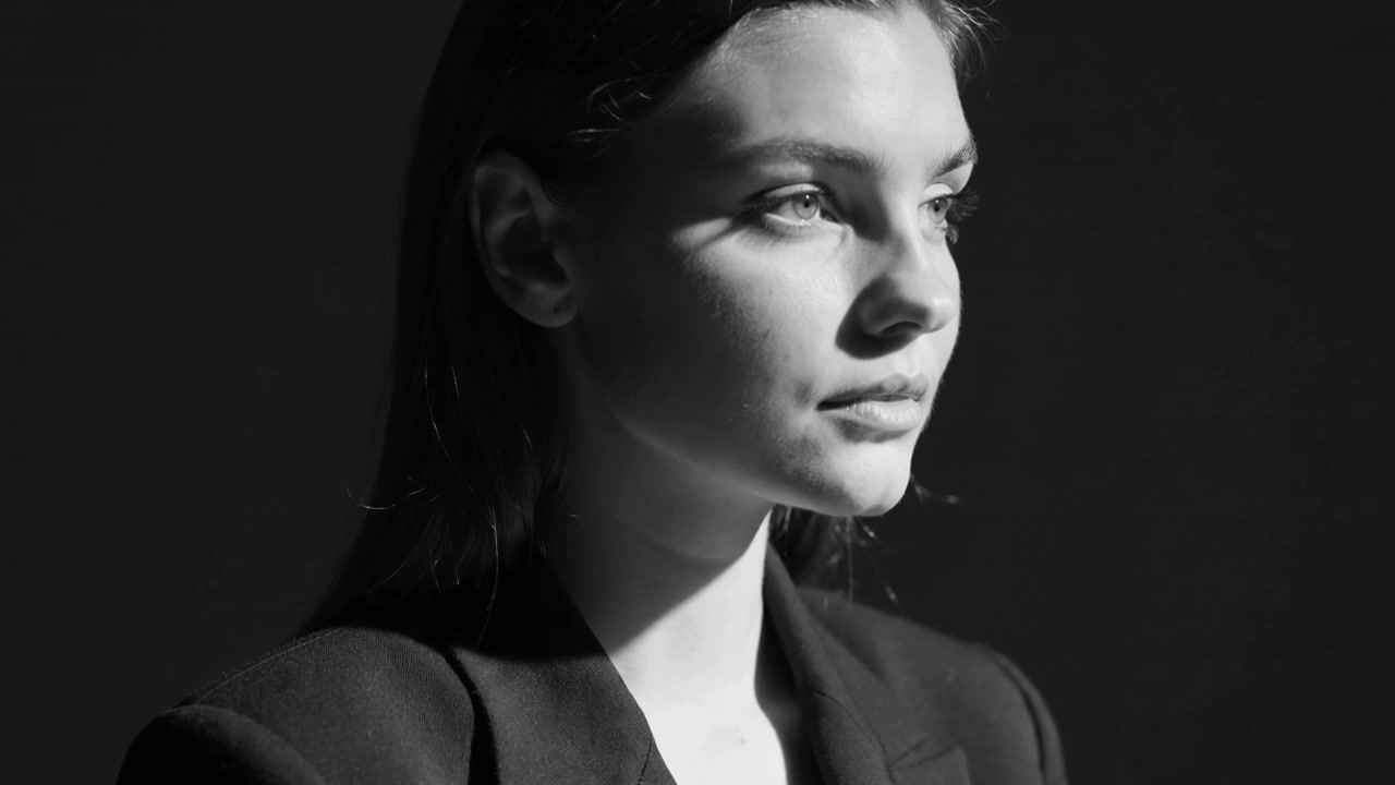 Modella che si gira, ruotando la testa a destra in studio, mostrando un blazer scuro, con luce principale fuori campo.