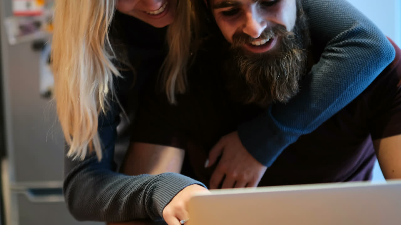 pareja abrazándose mientras usan una computadora portátil en casa 4k