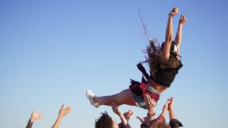 large group of young people lifting their female friend up in the air and throwing her up on raised hands. slow motion shot