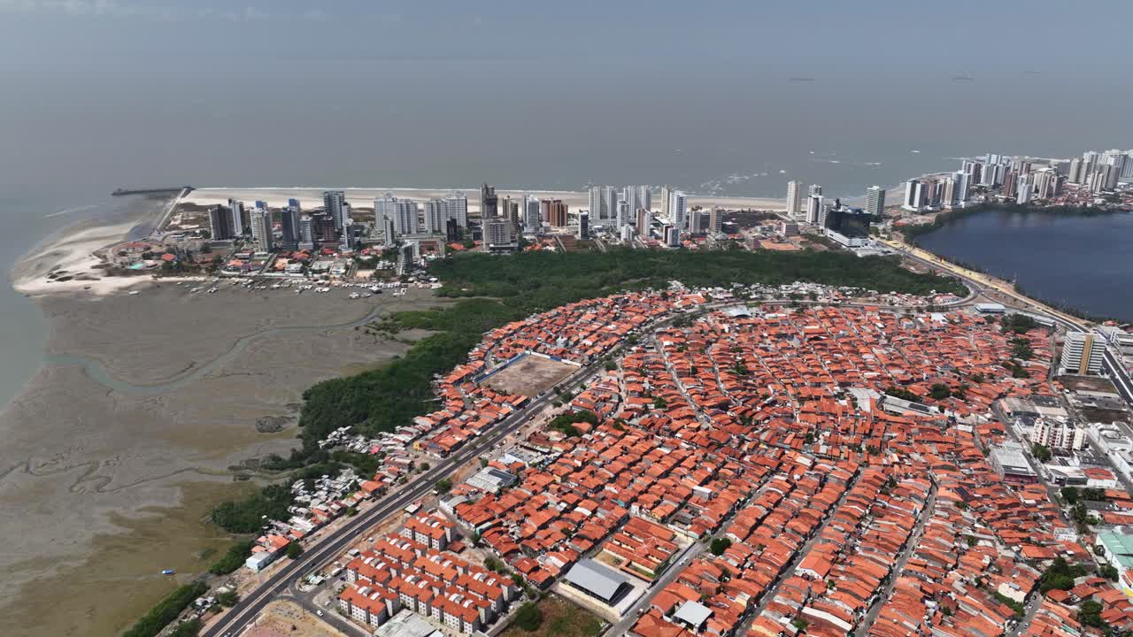 Sao Luiz favela, poor neighbourhood, slum or shantytown with Ponta D'Areia skyline buildings in background at Atlantic ocean coast, Maranhao, Drone shot