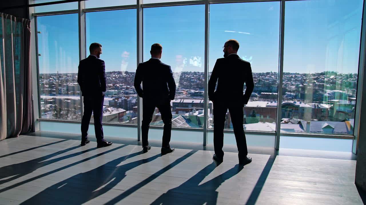 Funny businessmen in suits indoors. Office workers rest by the window. Business partners standing by the window and joyfully moving their bodies. Back view.