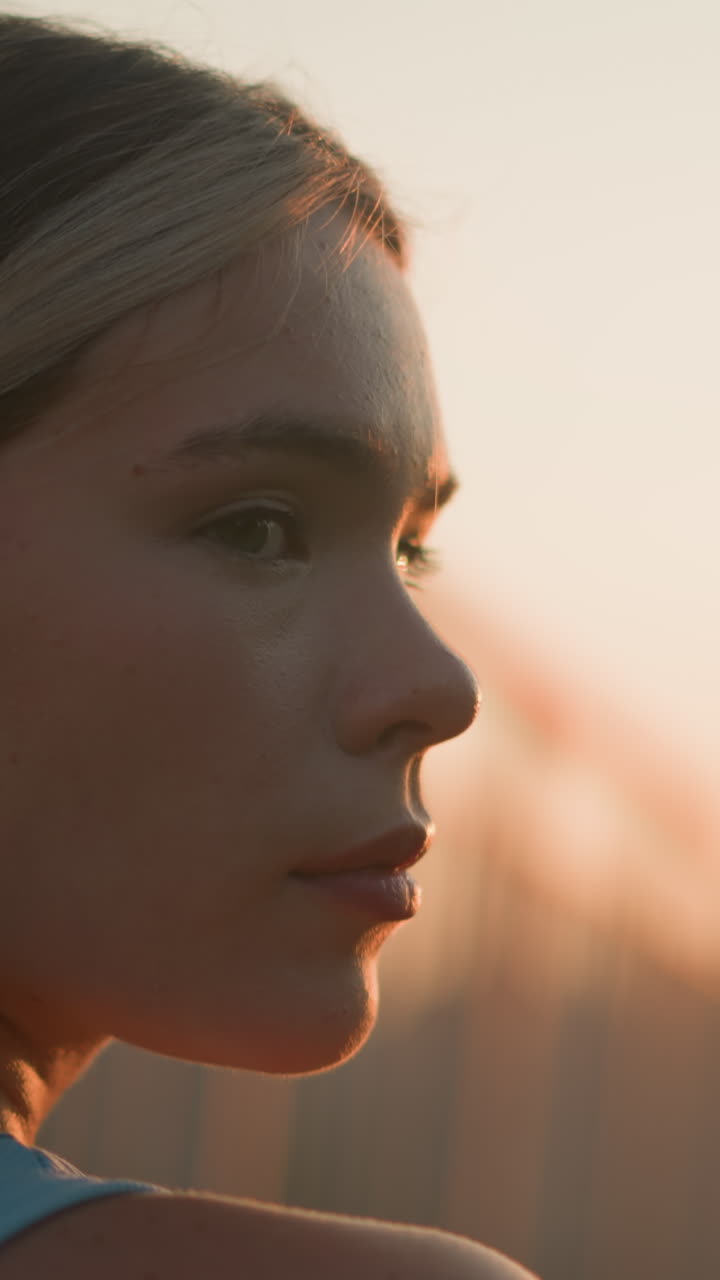 primer plano de una joven con una expresión de mal humor mirando hacia atrás mientras la luz del sol se refleja en su cara, sentada cerca de una barandilla de hierro por la noche