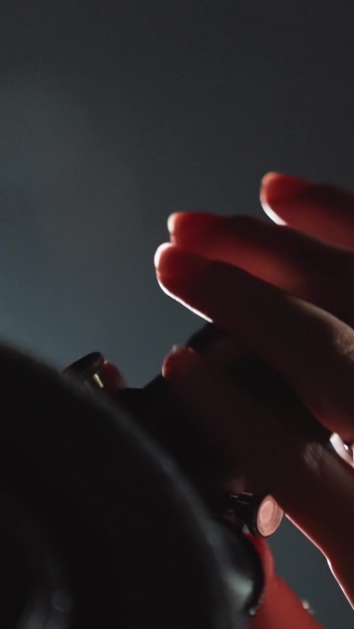 Pair of hands nails painted bright red manipulate unseen. Action continues smoothly indicating repeated fine tuning. Cylindrical object is seen at bottom right throughout