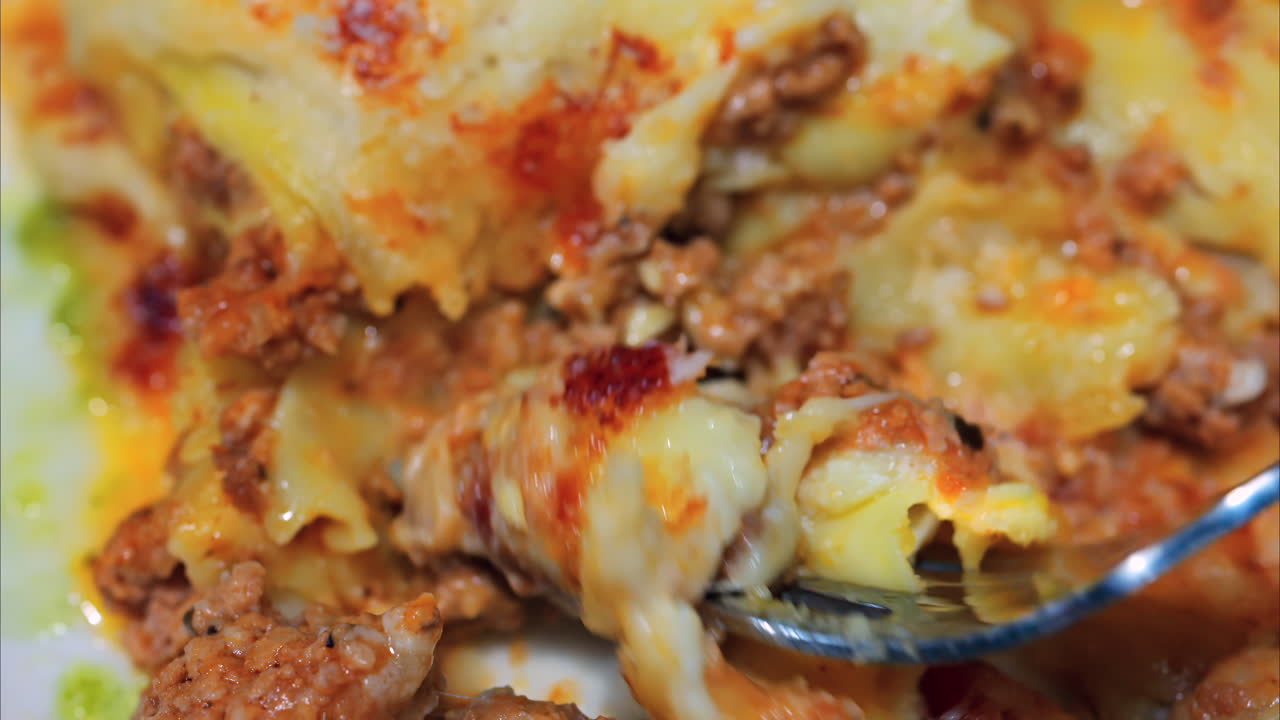 Close up of a fork picking up lasagna from a white plate