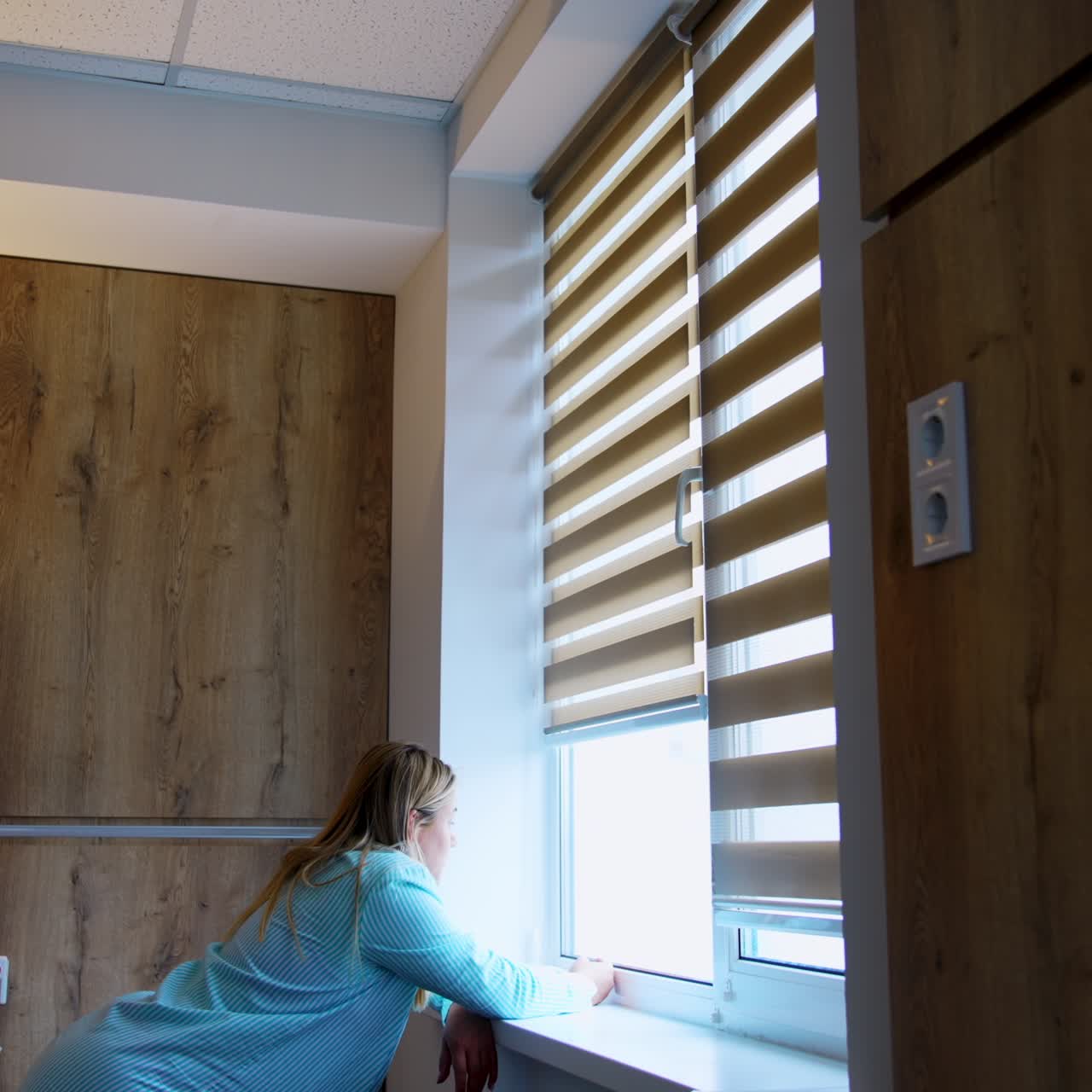 Caucasian woman stands leaned on the window-sill looking into window. Future mom in the maternity hospital ward