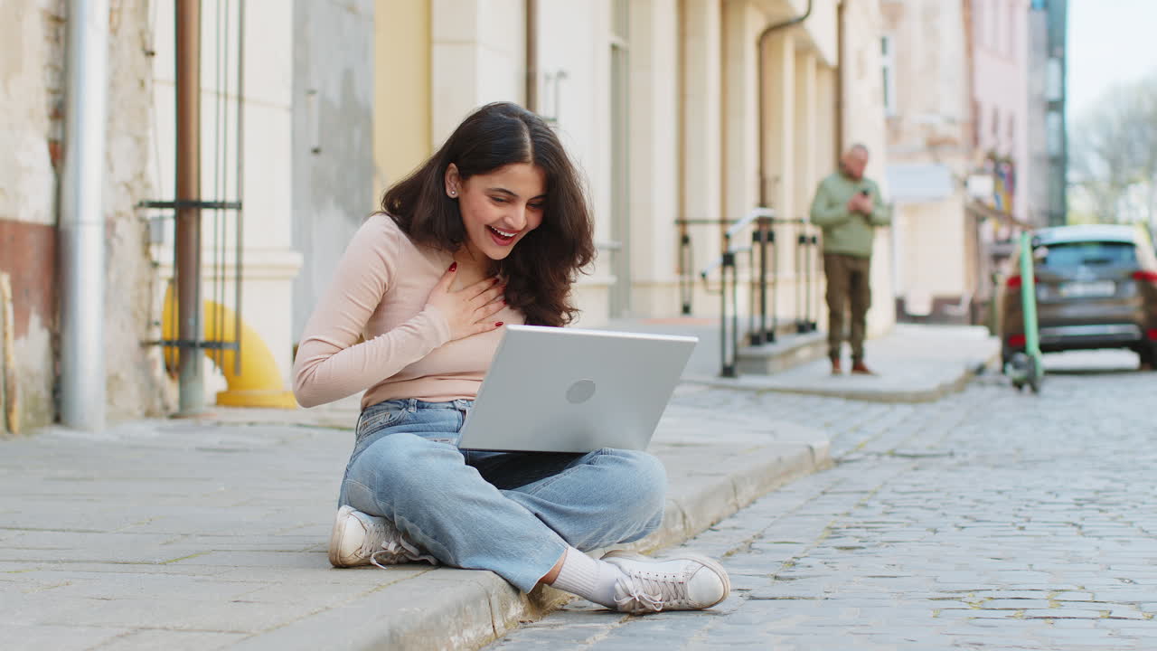 mujer india feliz trabajando en la computadora portátil celebrar el éxito ganar dinero sentado en la calle urbana en la ciudad