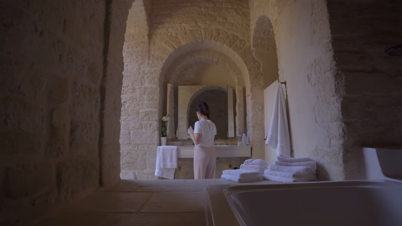 Woman getting ready in a unique stone bathroom with arched architecture