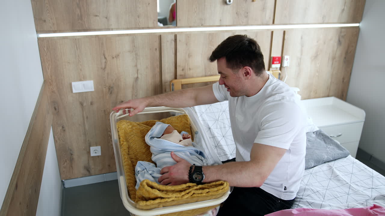 Happy dad sits over the crib with his newborn child. Father speaks to his little baby. Top view.