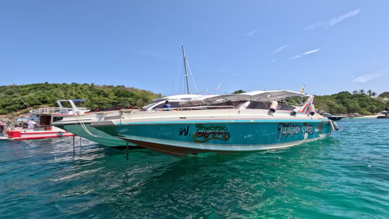 Turquoise speedboat glides across clear water, passing anchored boats under bright midday sunlight