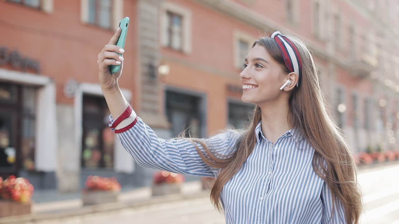 Giovane donna felice che si scatta un selfie o fa una videochiamata in una strada di città.