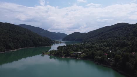 toma aérea en movimiento hacia adelante de los bosques montañosos que se encuentran con el lago limpio de paltinu del valle de doftana en rumania