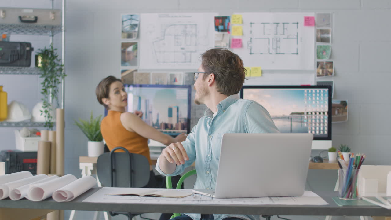 사무실에서 컴퓨터에 앉아 있는 남자와 여자 건축가들이 함께 모이기 위해 합류하고 있습니다.