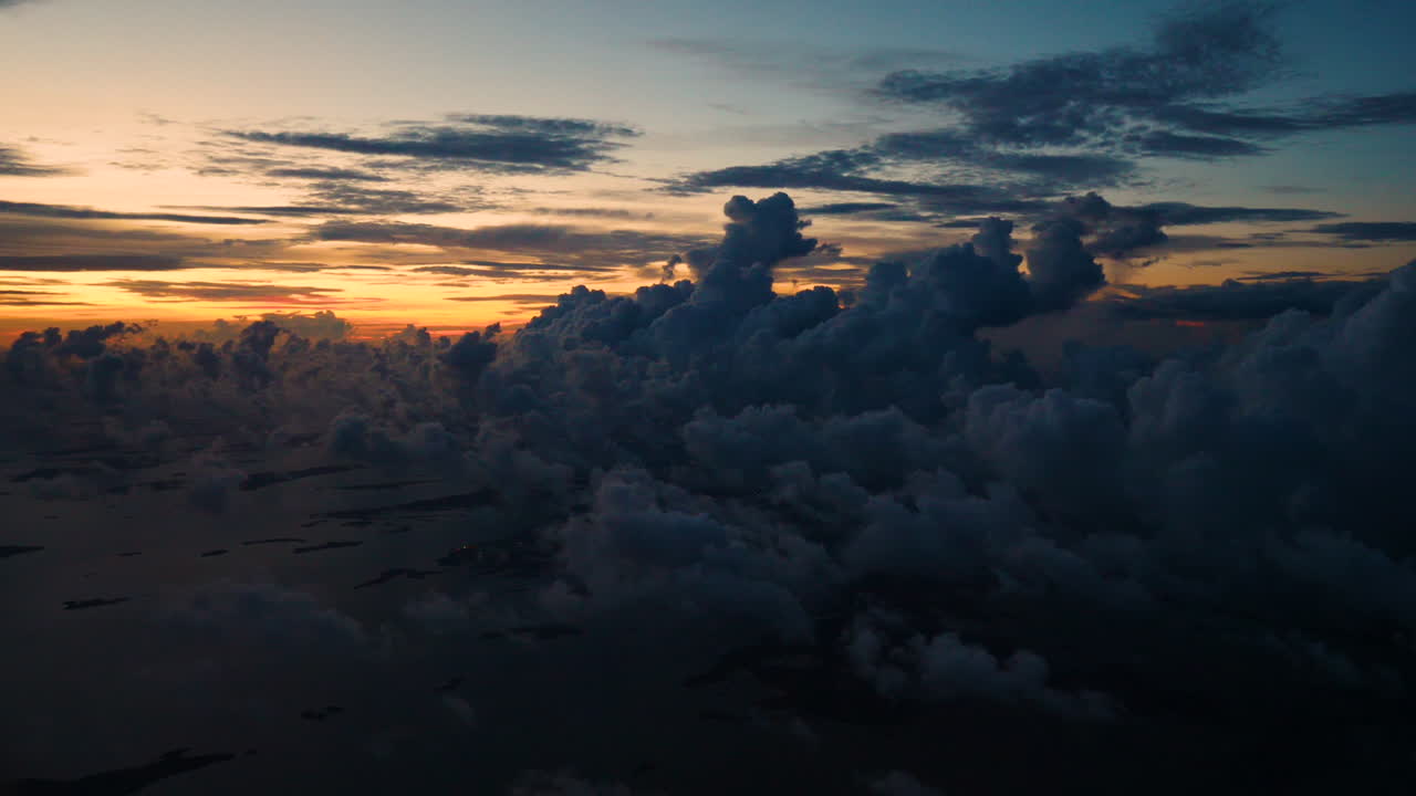 Slow motion video clip of the teal and orange sunset over the clouds, filmed from the window seat of a passenger airliner