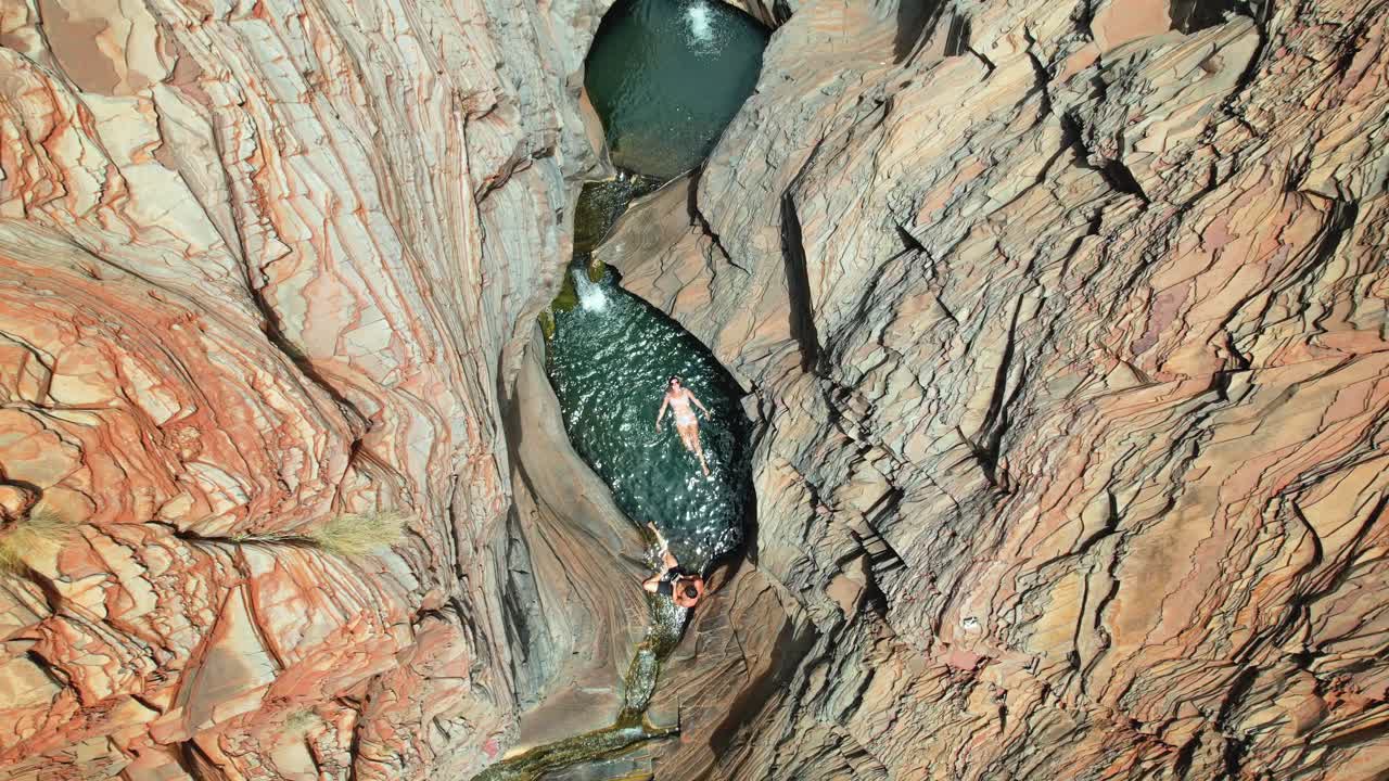 Aerial view of people swimming in natural pools within a narrow red rock gorge