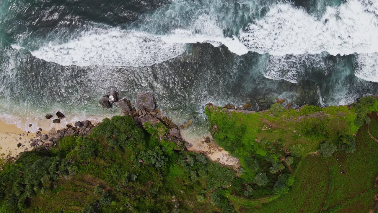 Overhead drone shot of Big waves on the beach hitting the rocky shore cliffs - Tropical beach of Indonesia