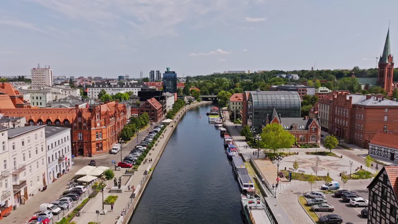 Drone moves forward over Brda River in Bydgoszcz Poland past boats and buildings