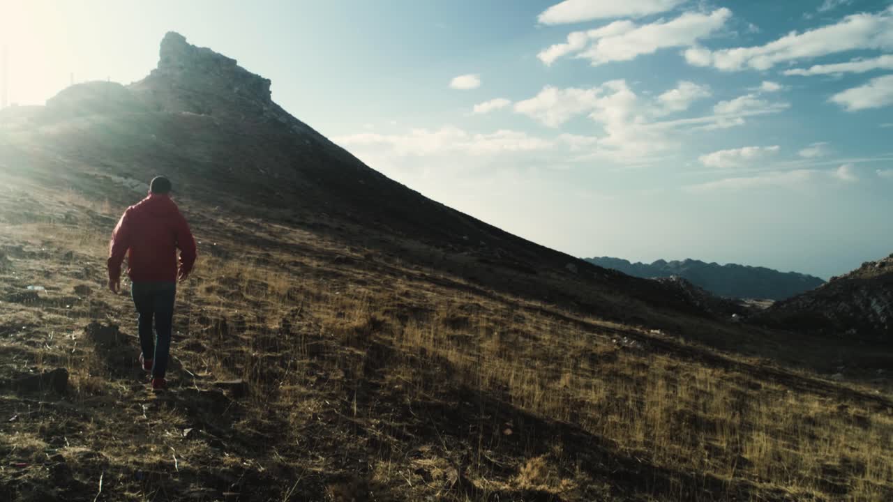 vista trasera de un hombre con chaqueta roja caminando hacia la montaña en el líbano, puesta de sol, tiro de seguimiento