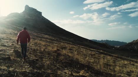 rear view of man in red jacket walking towards mountain in lebanon, sunset, tracking shot