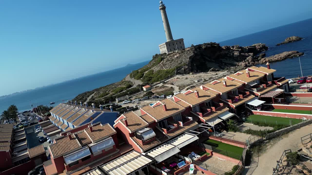 A dynamic drone zooms in, capturing cinematic shots of a city filled with low-rise housing estates, anchored by a prominent lighthouse standing near the coast.