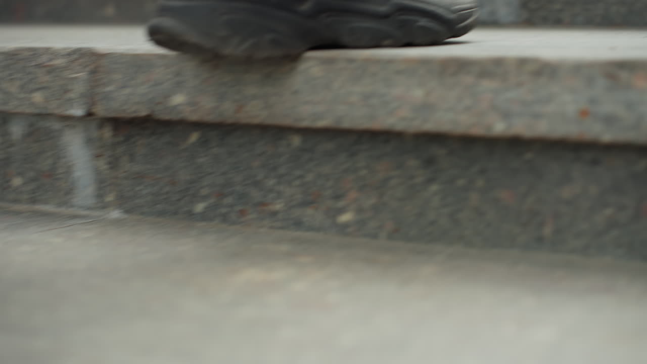 closeup sneakers climbing stone stairs, denim jeans visible, worn black shoes stepping on concrete, slow steady pace, textured granite edges, urban commute mood, cinematic muted tones, morning