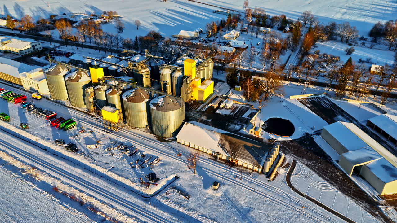 Golden hour glow over snow covered silos and storage buildings beside train tracks