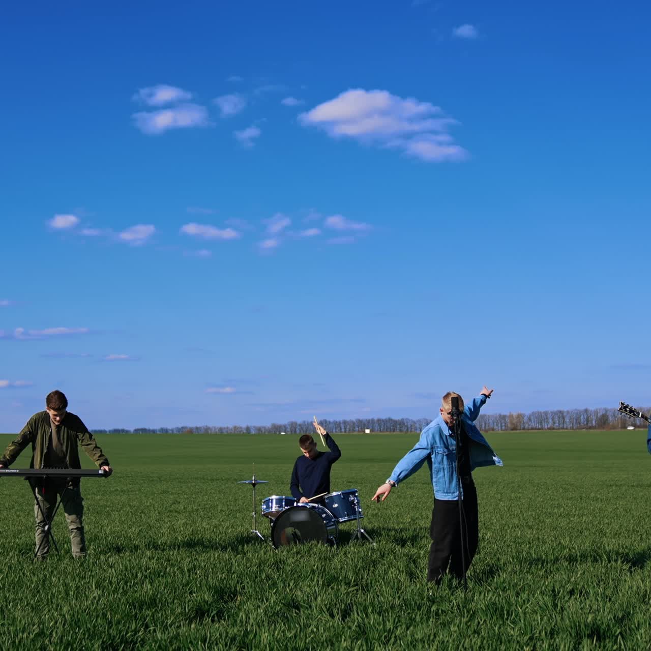 Young musical band giving a concert on field. Friends perform music with musical instruments under blue sky. Outdoor entertainment