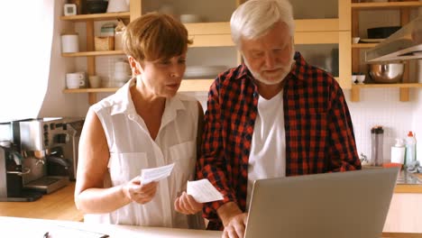 senior couple paying bills online on laptop in kitchen