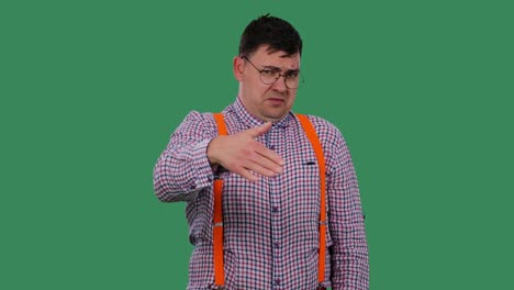 portrait of a man looking at someone and waving his hand, showing a go away gesture. a man with glasses, a shirt with orange suspenders in the studio on a green screen. slow motion. close up