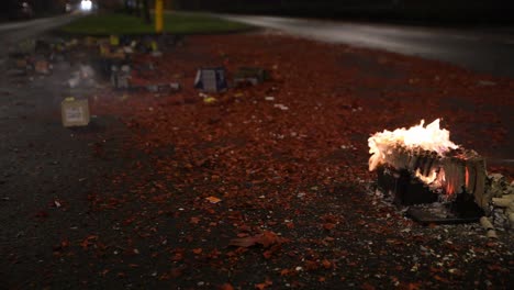 flame on fireworks burn out in the middle of the street as cars drive by and debris fills the roadway