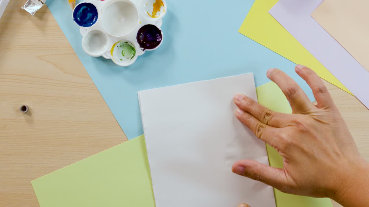 Hands fold paper over wet paint to create a symmetrical watercolor Rorschach inkblot design