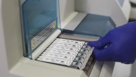 female hand in blue gloves inserts test catridge into analytical automatic machine to perform test. lab chemistry or science research and development concept.