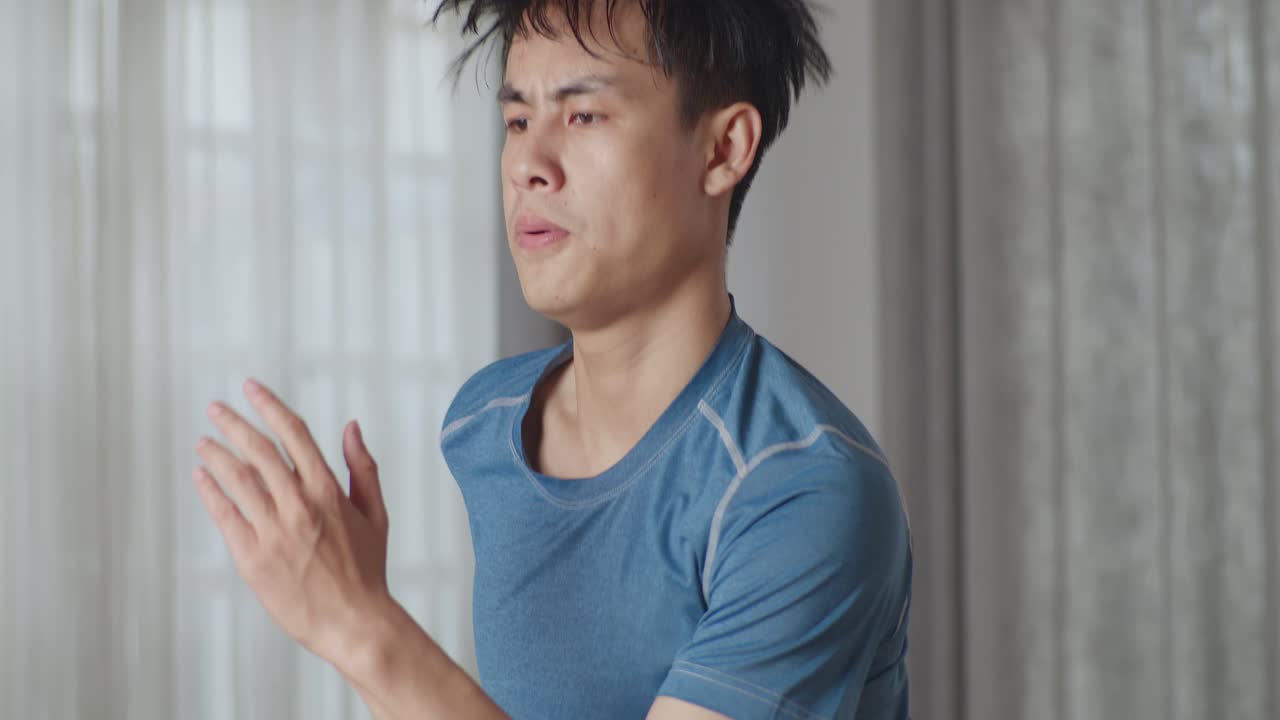 스포츠 의류를 입은 아시아 운동 피트니스 남자가 현대적인 인테리어와 함께 그의 거실에서 활기차게 조하고 있습니다.