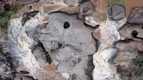 aerial top down view of water flows over the stones in green forest