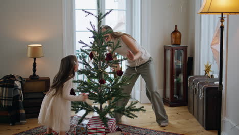 familia jugando en la habitación del árbol de año nuevo. madre emocional escondiéndose de su hija