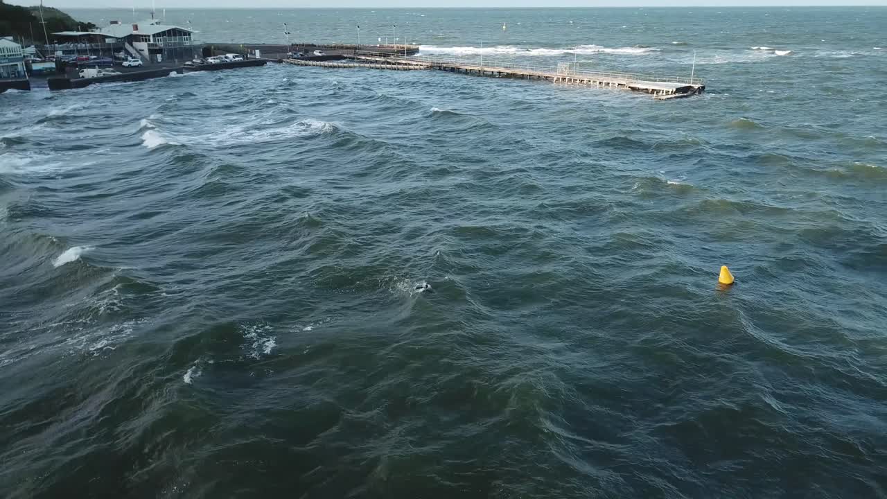 drone antena sobre el océano en melbourne ondulado ventoso día nublado con hombre nadando