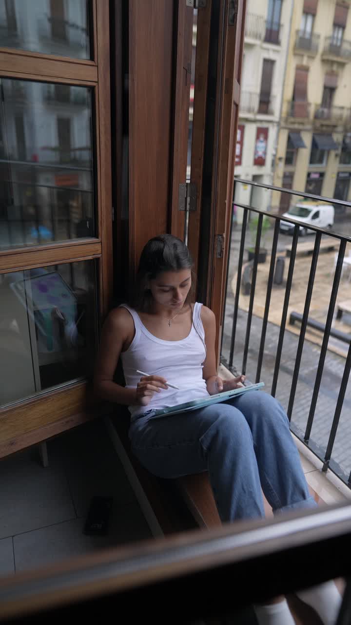 mujer dibujando en una tableta digital junto a la ventana