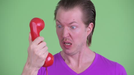 zoom in shot of young man screaming to old telephone against green background