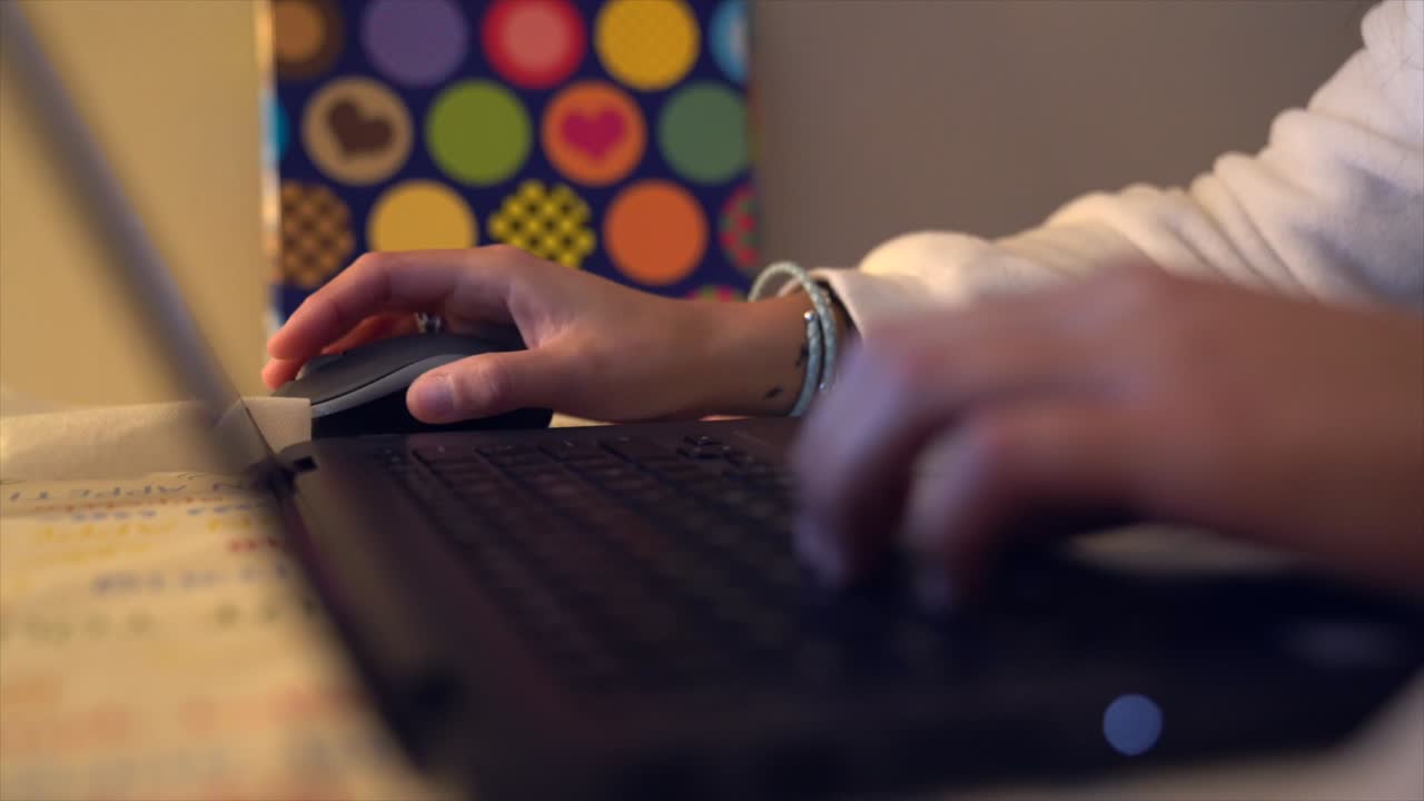 persona haciendo clic con el mouse y escribiendo en un teclado en una computadora negra y una carpeta colorida en el fondo