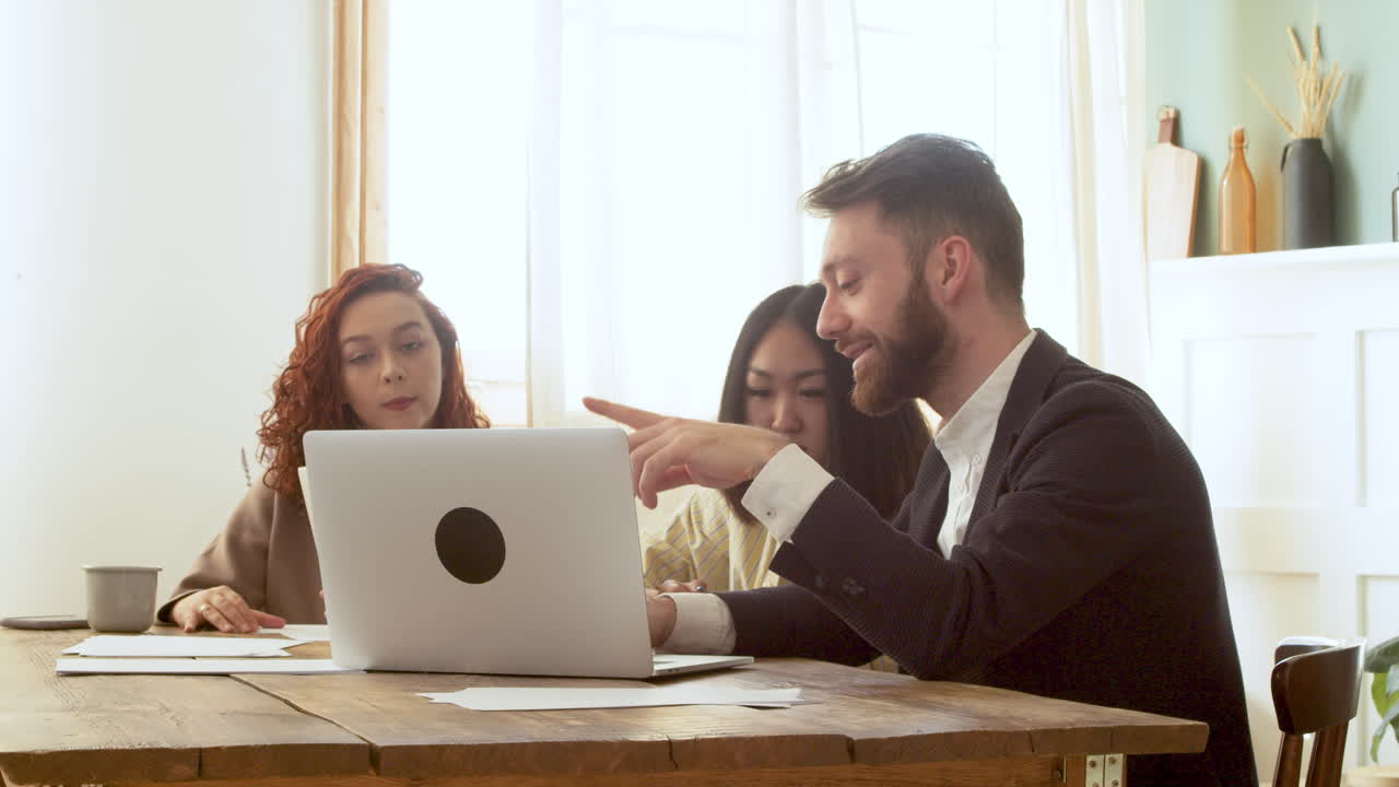 equipo de negocios multiétnico sentado en la mesa y teniendo un debate mientras mira la computadora portátil